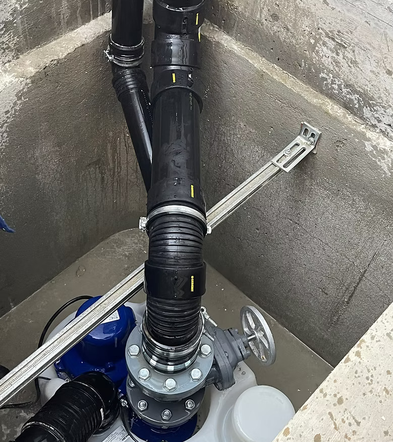 Unterirdische Rohrleitungen und Ventil in Betonkammer, mit schwarzen und blauen Komponenten.