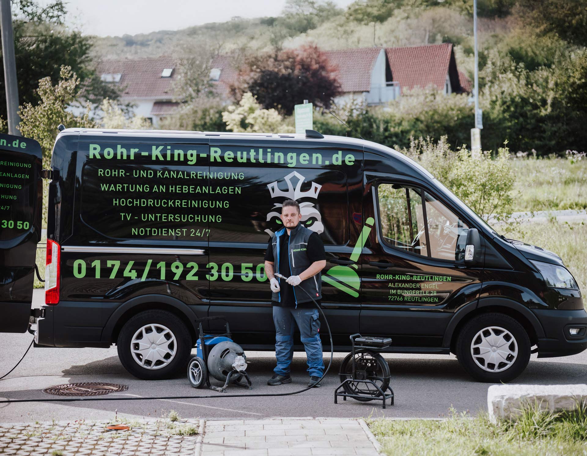 Ein lächelnder Mann in Arbeitskleidung steht vor einem schwarzen Firmenwagen.